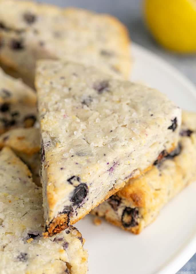 Blueberry lemon scones piled on white serving platter with lemon in background