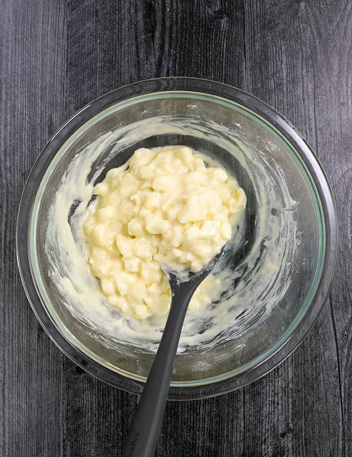 Gluten free apple fritter batter in a glass bowl with a mixing spoon