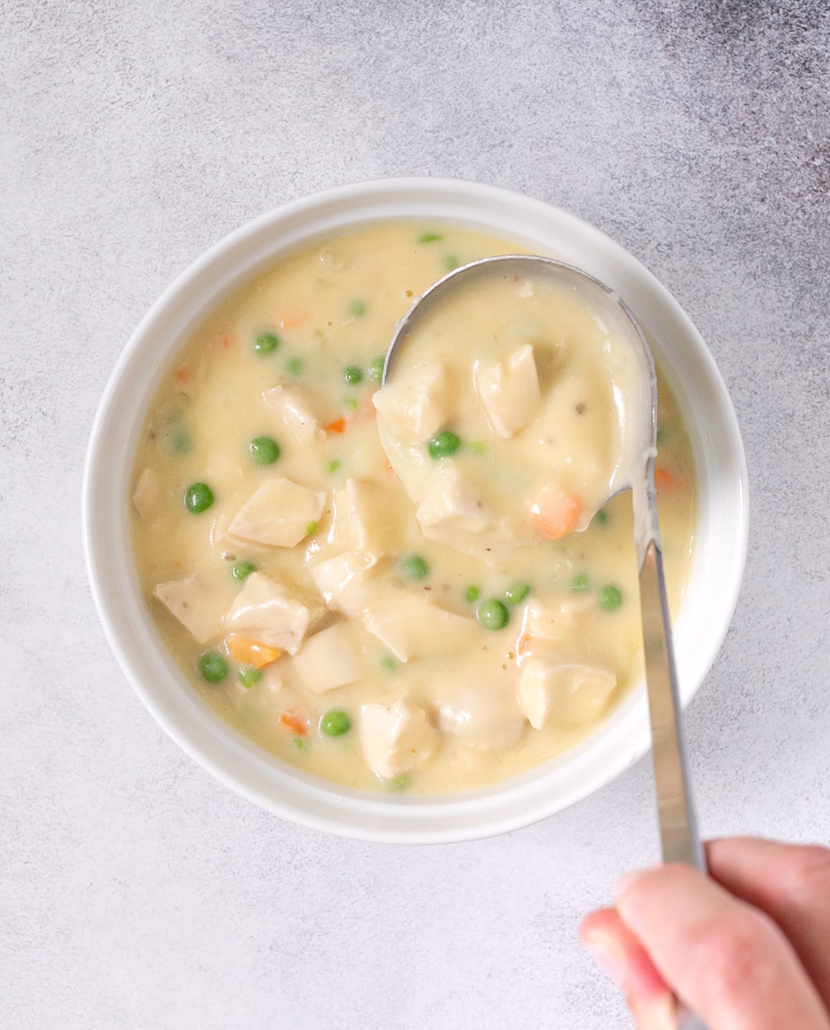 Ladle placing chicken pot pie filling into white casserole dish