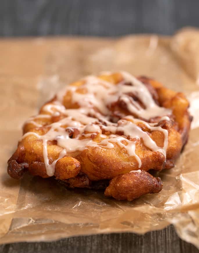 One apple fritter with glaze on waxed paper