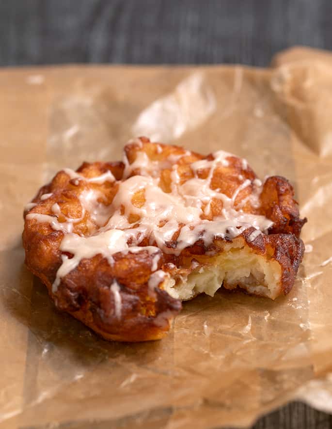 One glazed apple fritter on waxed paper with a bite