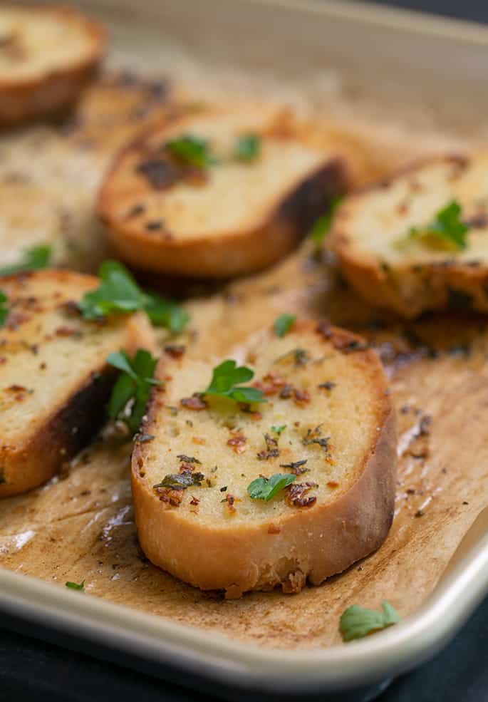 Pieces of garlic bread on baking sheet with fresh parsley leaves