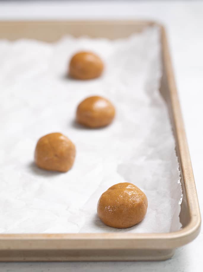 Raw balls of gingersnap dough on white paper on a tray