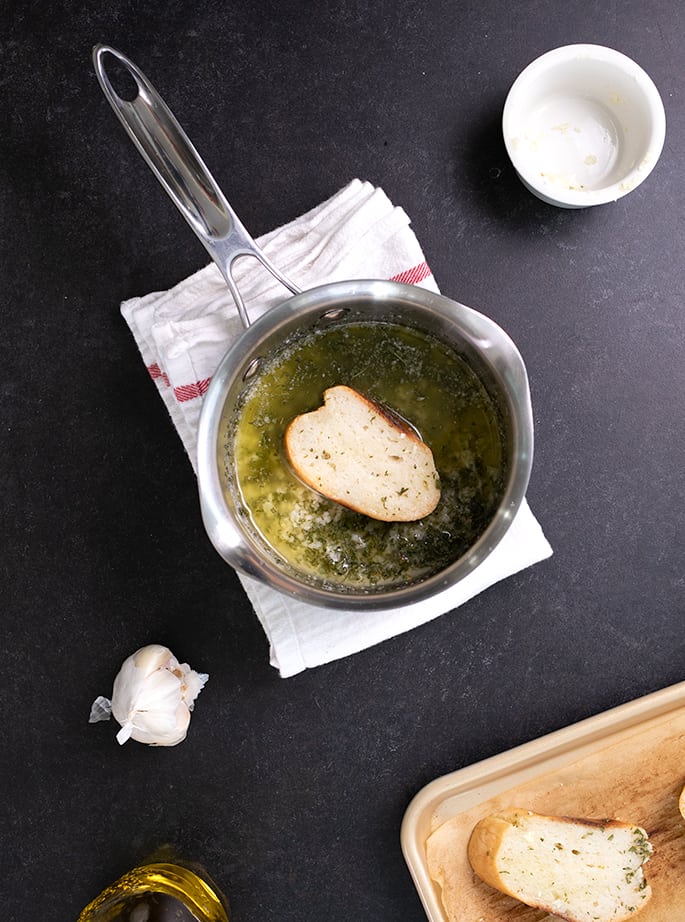 Sliced French bread being dipped in garlic butter