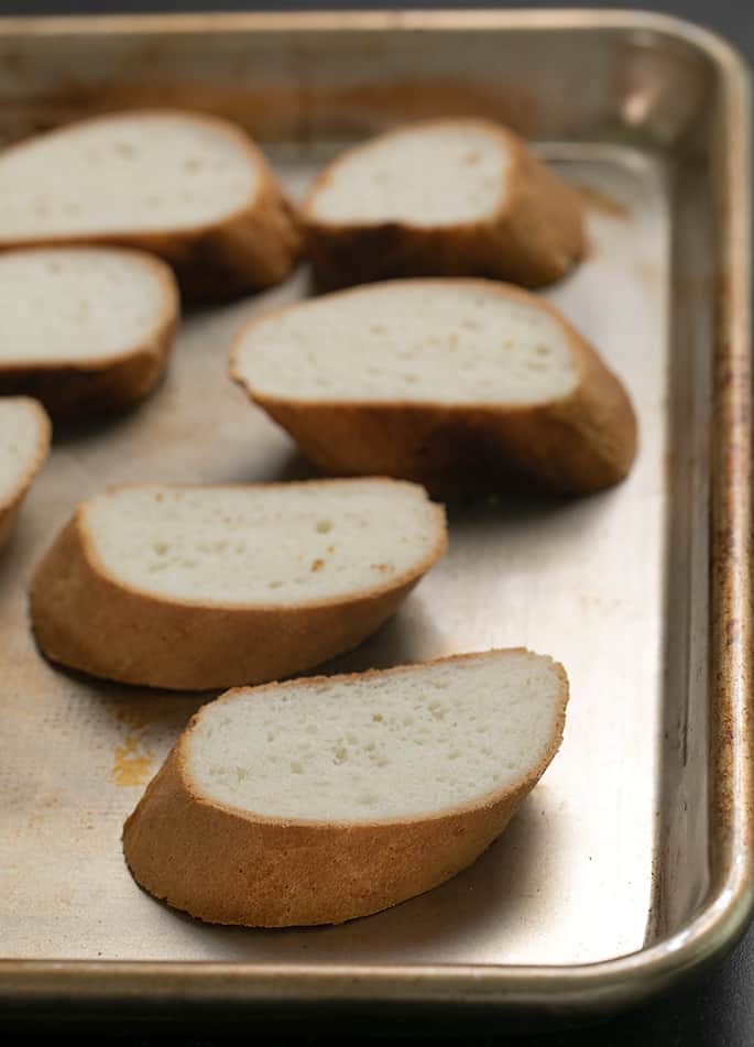 Sliced pieces of French bread on a baking sheet