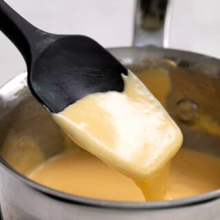 Cheese sauce falling off black spatula into saucepan