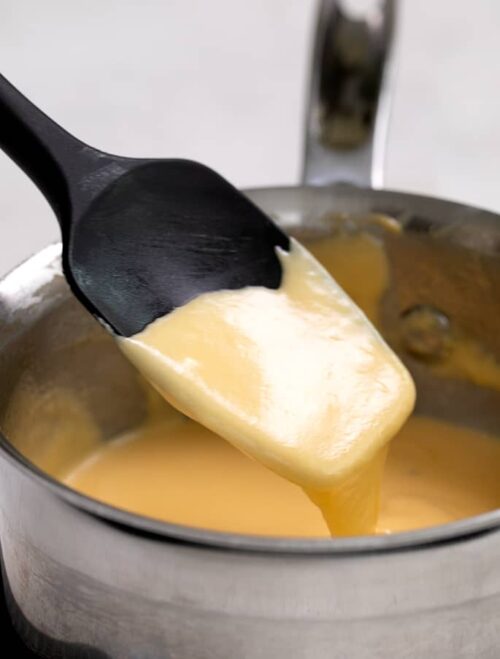 Cheese sauce falling off black spatula into saucepan