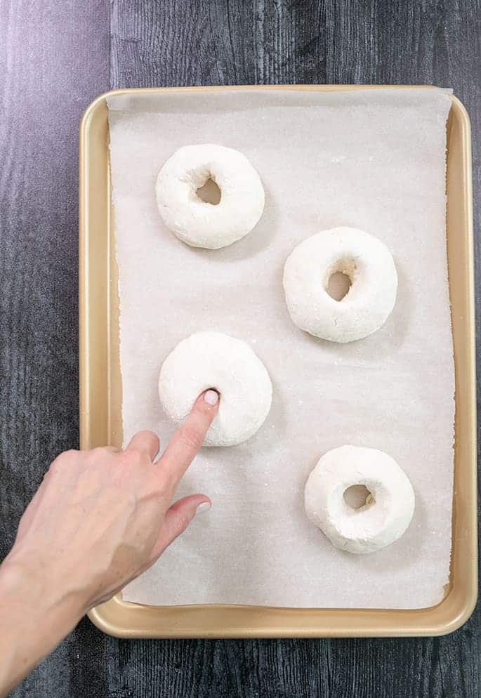 Finger poking a hole in a round of raw bread dough on a tray