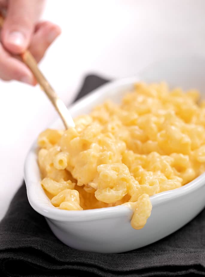 Hand holding a fork lifting macaroni and cheese from a narrow white bowl