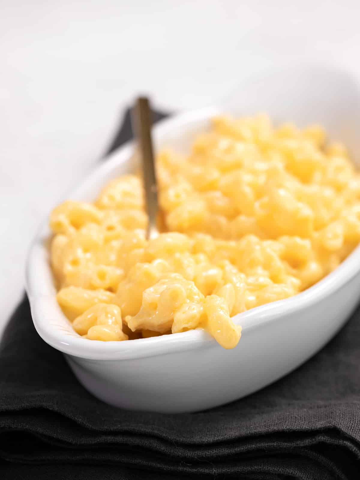 Macaroni and cheese in a white boat with a fork, on a dark gray napkin
