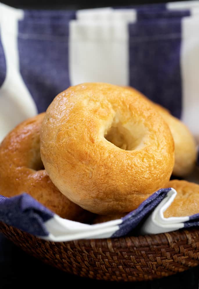 Plain light brown round bread with center holes in a brown bowl with a blue and white stripe towel