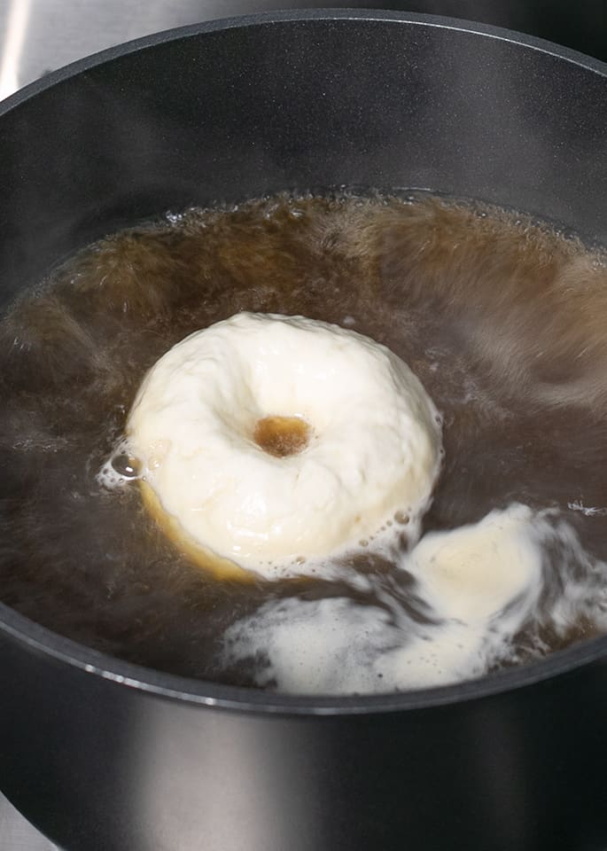 Raw round bread with a center hole boiling in water in black pot