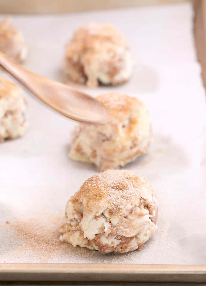 Spoon sprinkling cinnamon sugar on raw mound of cinnamon sugar biscuit