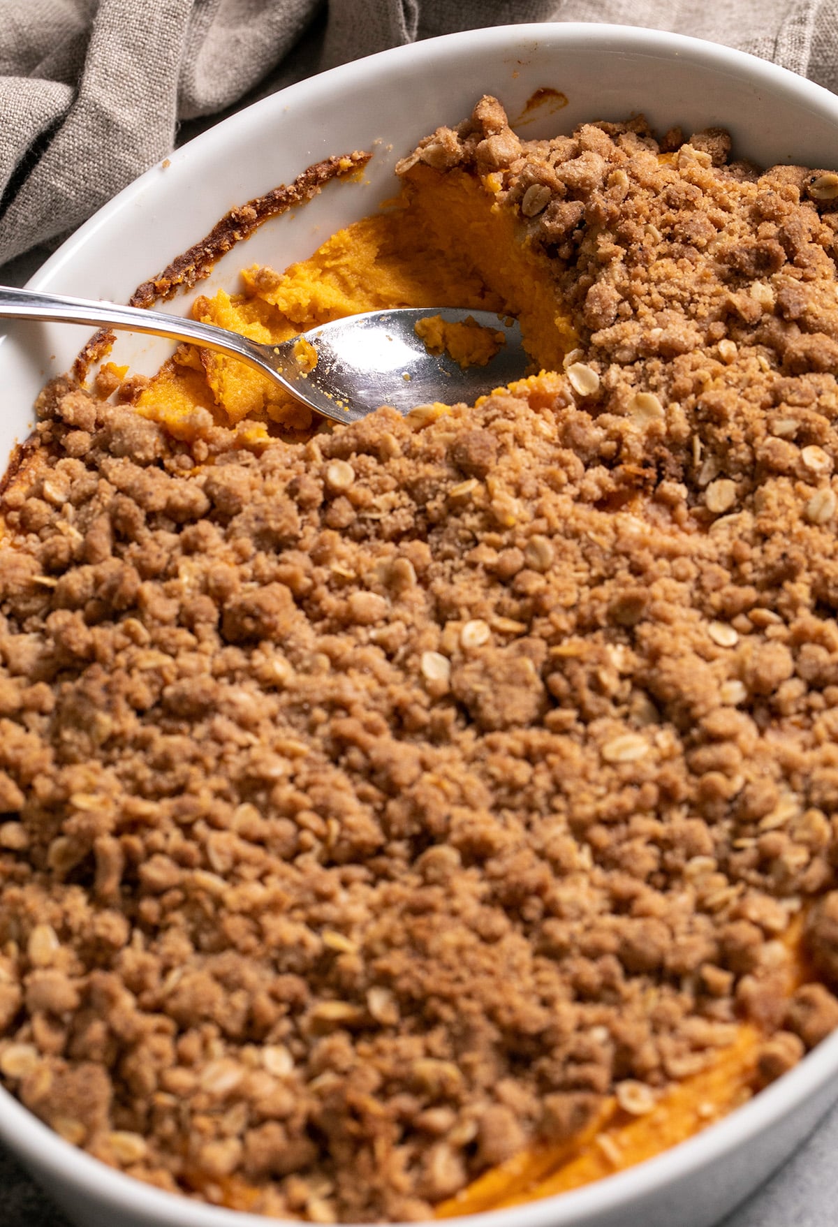 Sweet potato casserole in white baking dish with spoonful missing