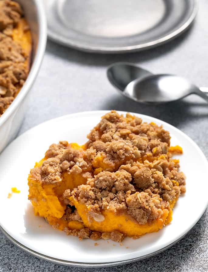 Sweet potato casserole serving on small white plate with spoons and serving dish