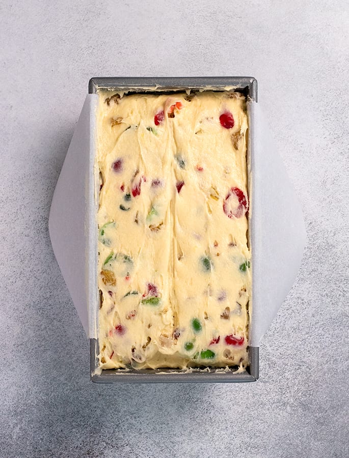 White fruit cake batter in pan lined with white paper overhead image