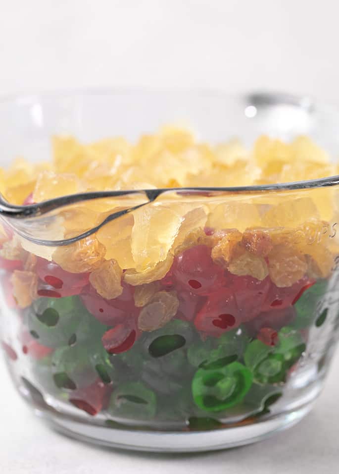 large glass measuring cup filled with yellow, green, and red candied fruit