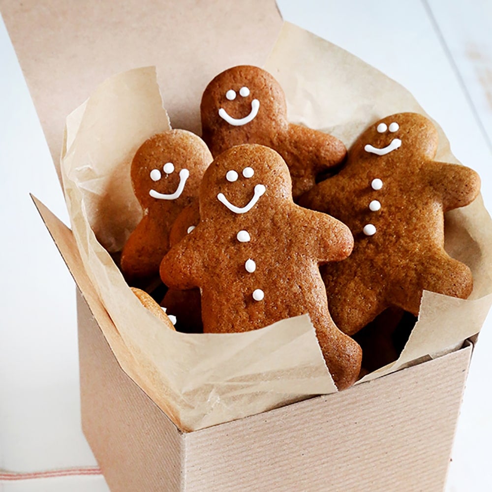 4 gluten free gingerbread men cookies propped up in brown kraft box with brown paper liner