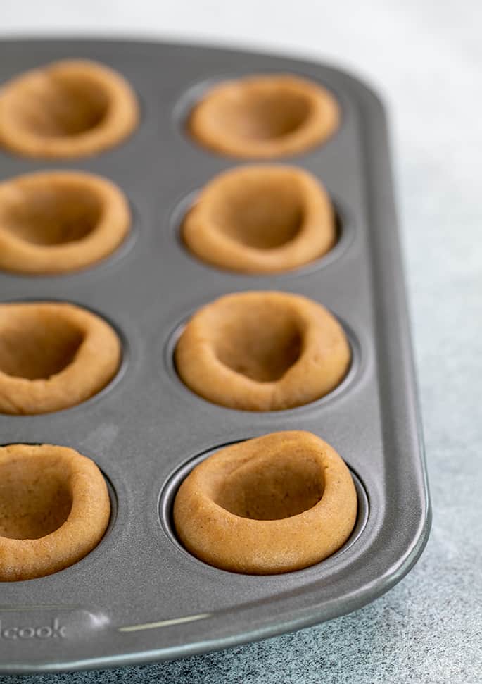 Raw gingerbread cup dough with holes in center in mini muffin tin