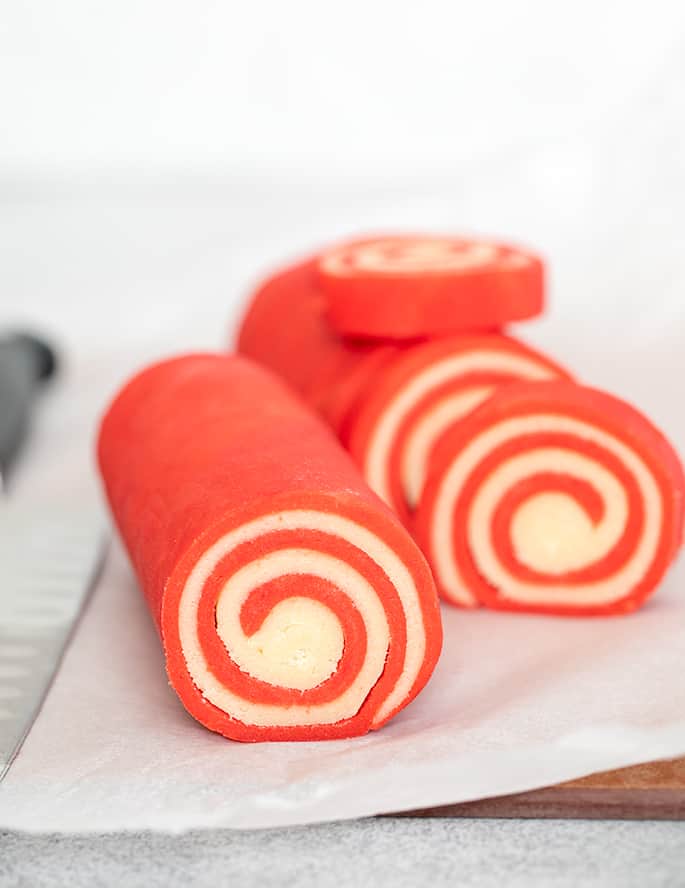 Red and white raw pinwheel cookie dough cut partially into slices