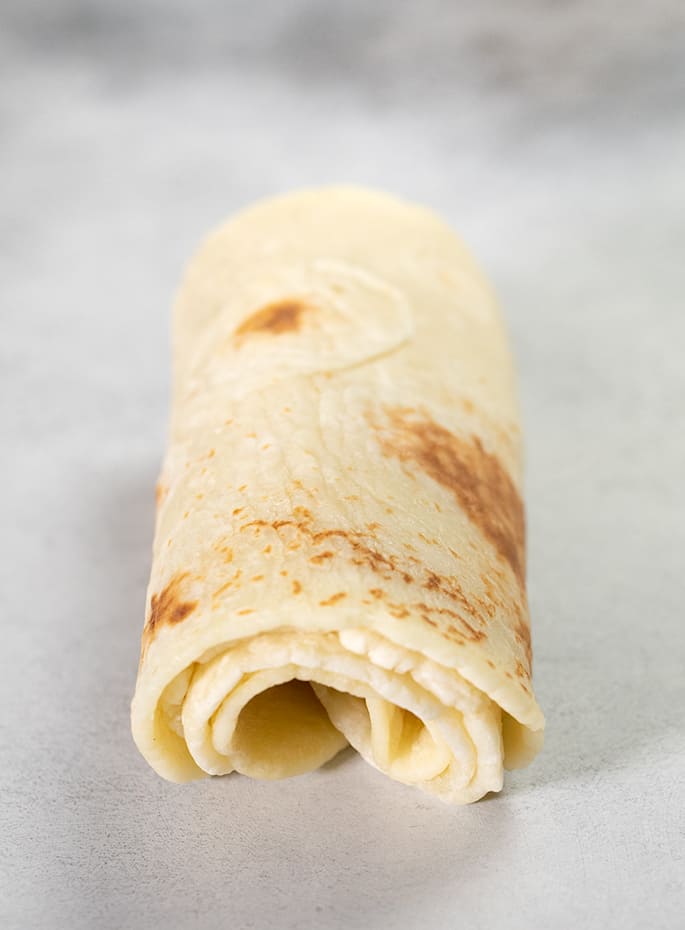 3 tightly rolled flatbreads on a white surface