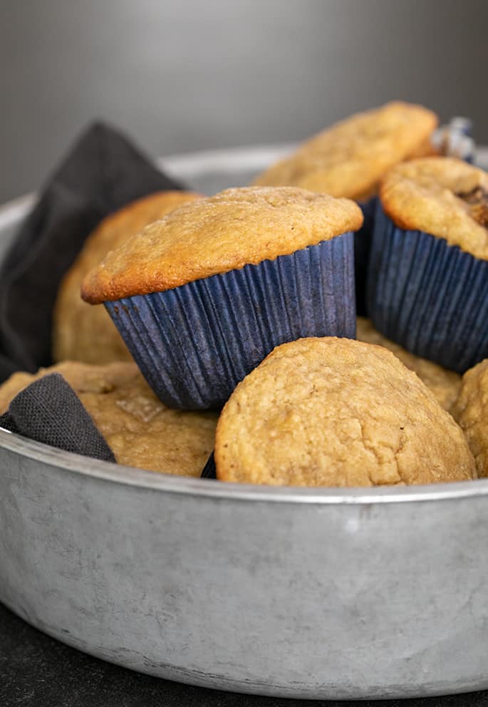 Almond flour muffins in blue liners in a pile in a round metal tin with dark gray cloth liner