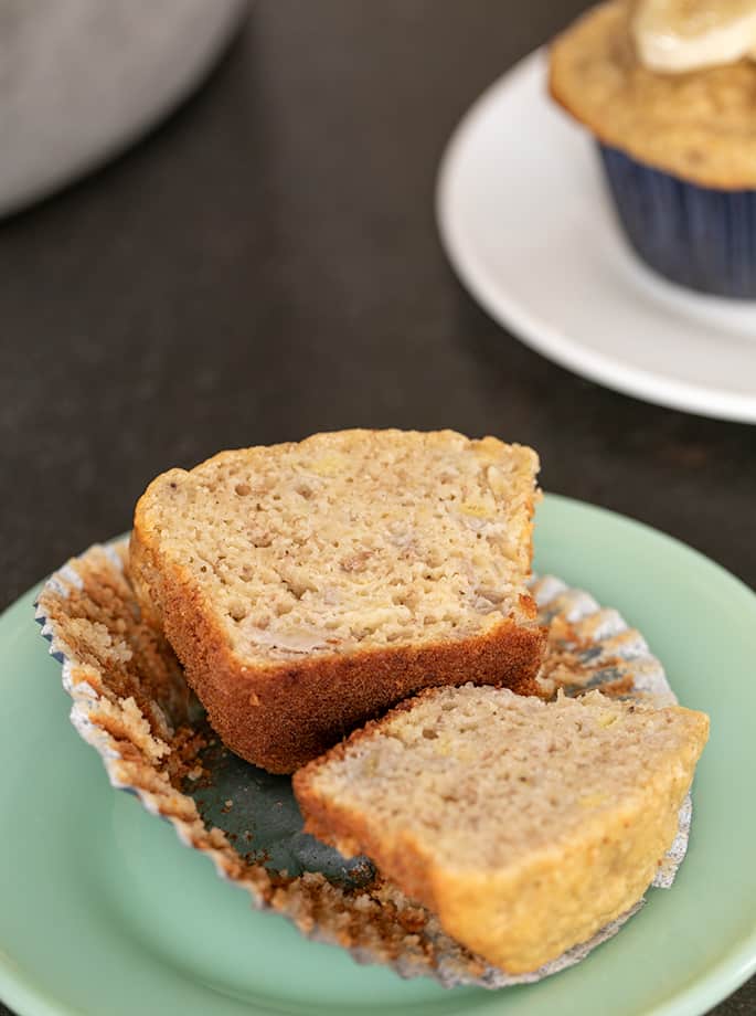 Banana muffin sliced in half on small green plate with muffin on small white plate in background