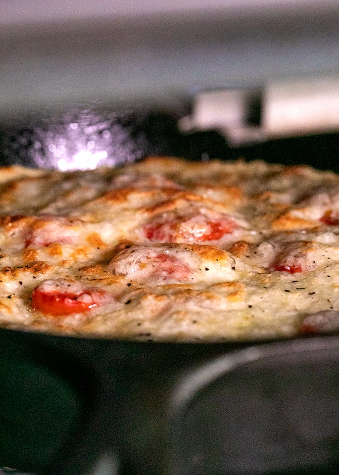 Chickpea pizza in cast iron skillet under oven's broiler