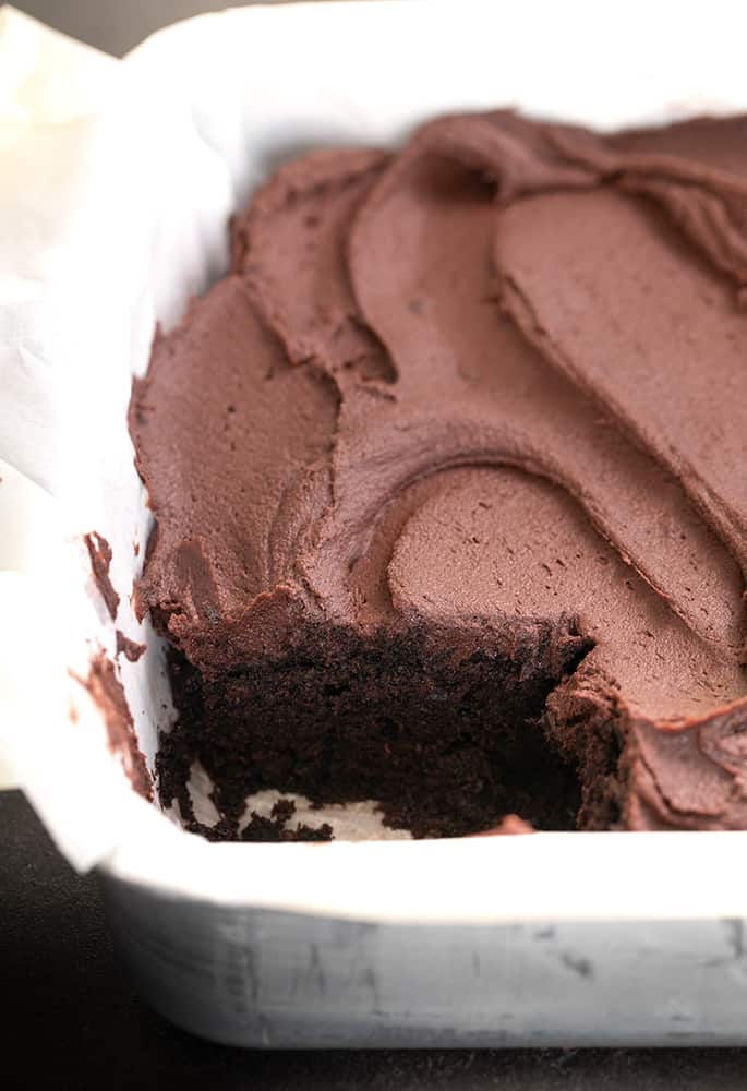 Chocolate frosted chocolate cake in square baking pan with one piece missing