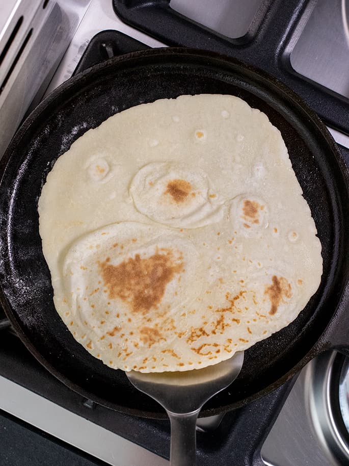 Flatbread on metal spatula in cast iron skillet