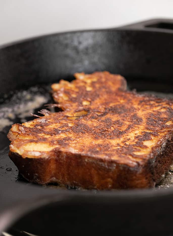 French toast slice frying in butter in black cast iron pan