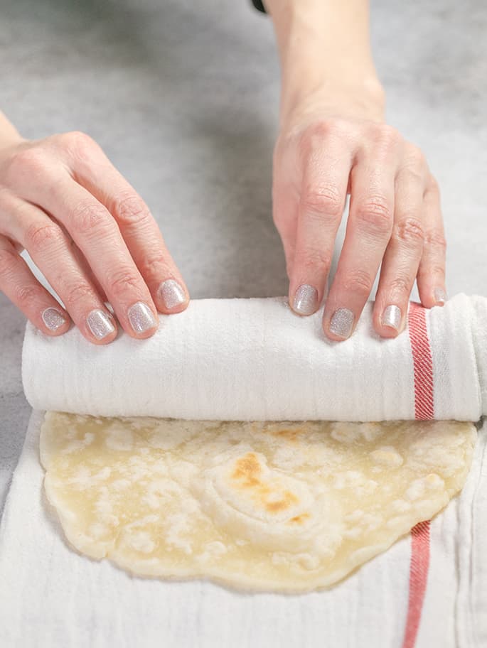 Hands rolling flatbread in a white towel with a red stripe