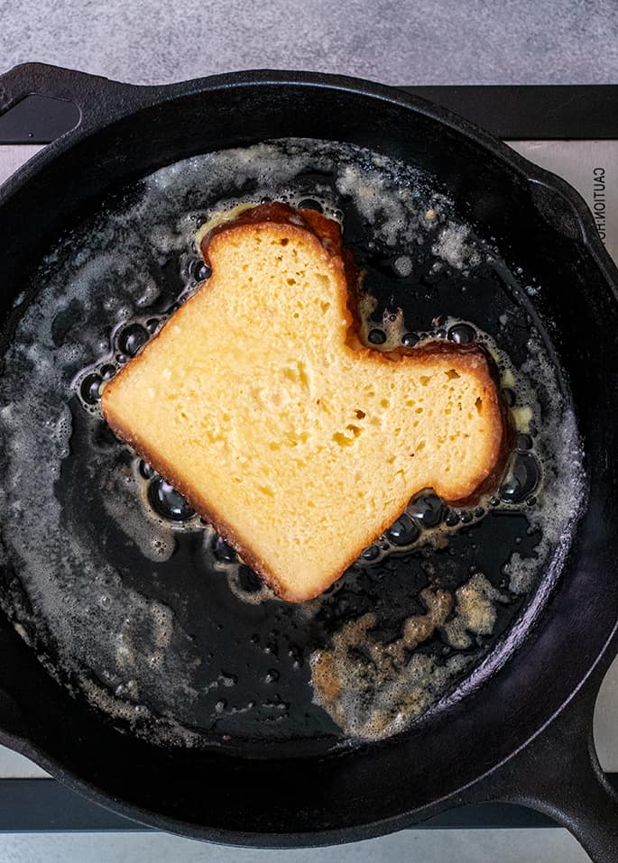 Overhead image of one slice of bread frying in a cast iron skillet with butter