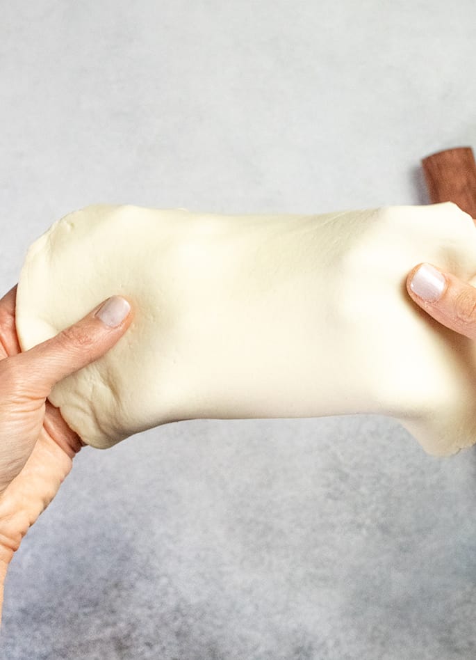 Overhead image of two hands holding a piece of raw flat dough