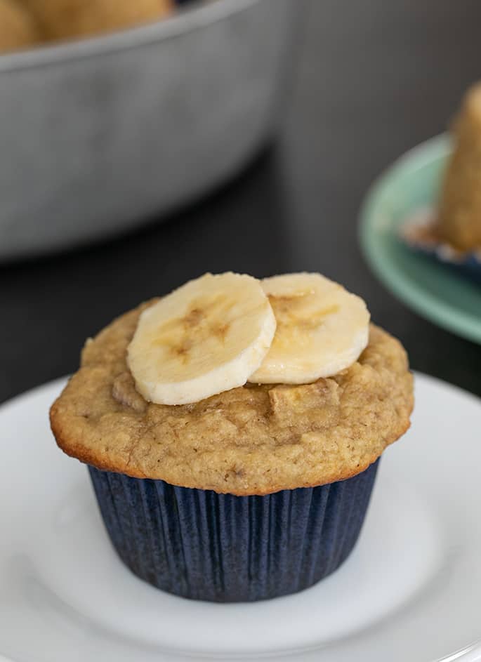 Whole almond flour muffin on small white plate with two banana slices on top