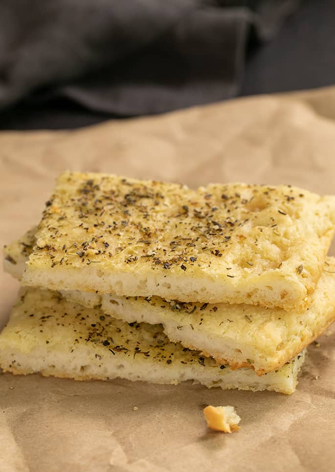 side image of 3 pieces of herb focaccia on brown paper with a large crumb