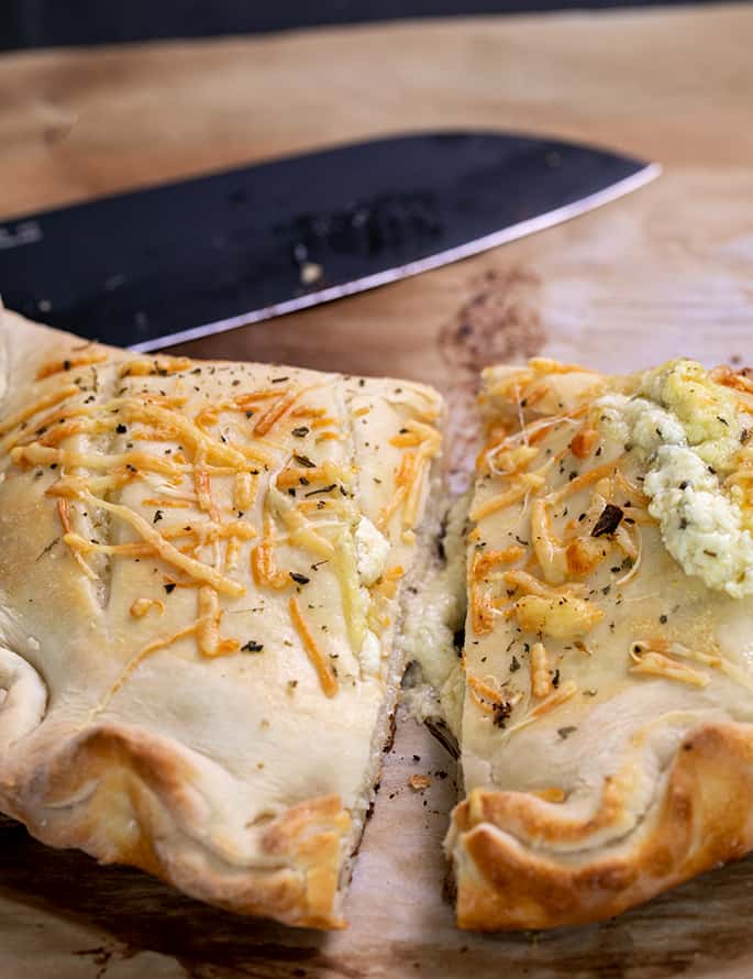 Baked calzone cut in half with black santoku knife in background on brown paper