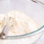 Glass bowl filled with white flour and a whisk