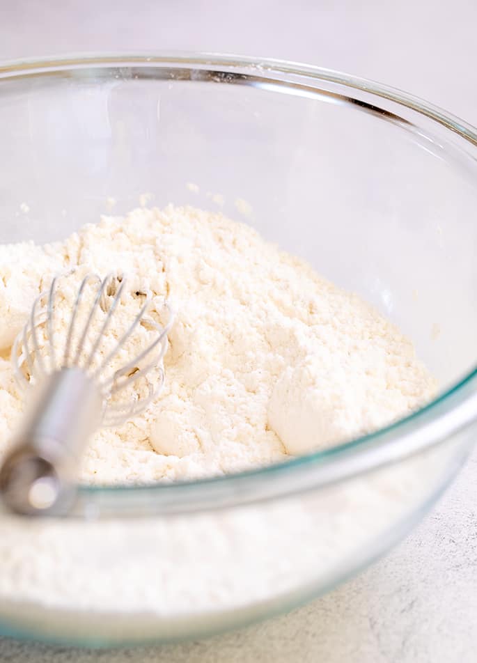 Glass bowl filled with white flour and a whisk