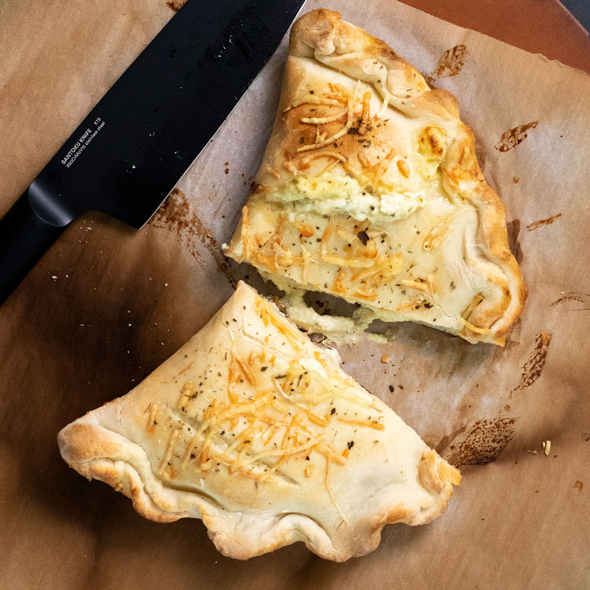 gluten free calzone cut in half on brown paper with black knife