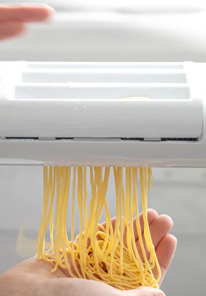 Hand below pasta roller catching cut fresh angel hair pasta noodles