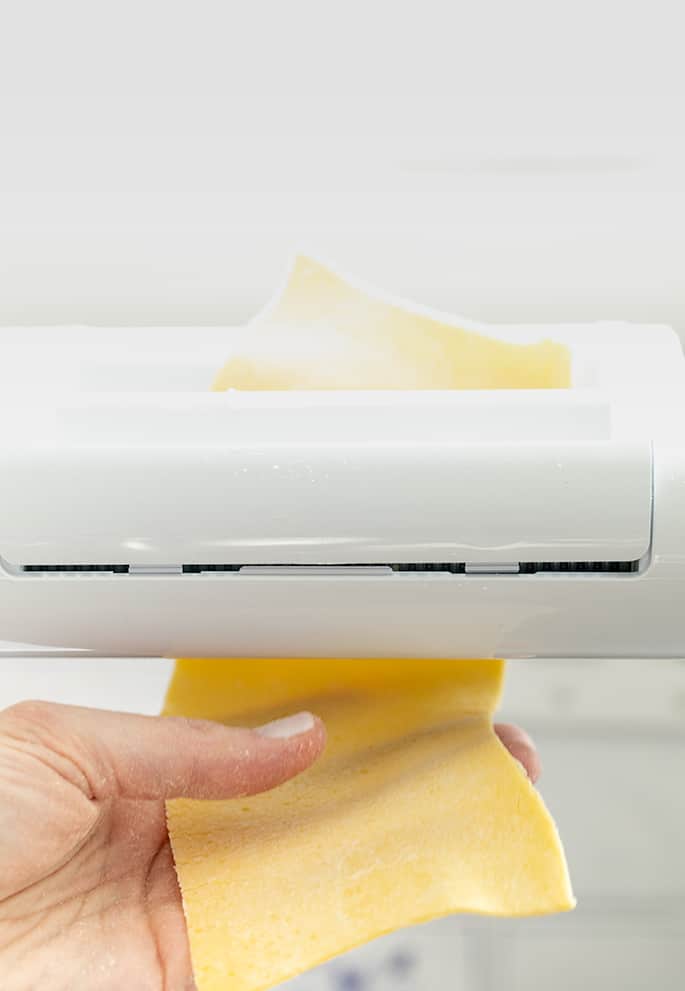 Hand catching rectangle of pasta dough coming out of pasta roller