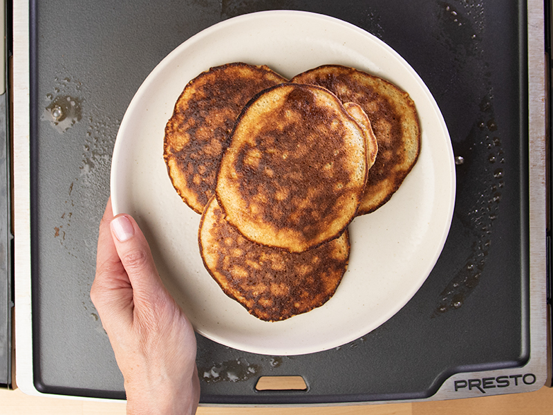 Hand holding white round plate with 4 banana pancakes