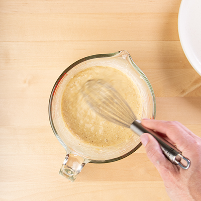 Whisk mixing banana pancakes batter in measuring cup