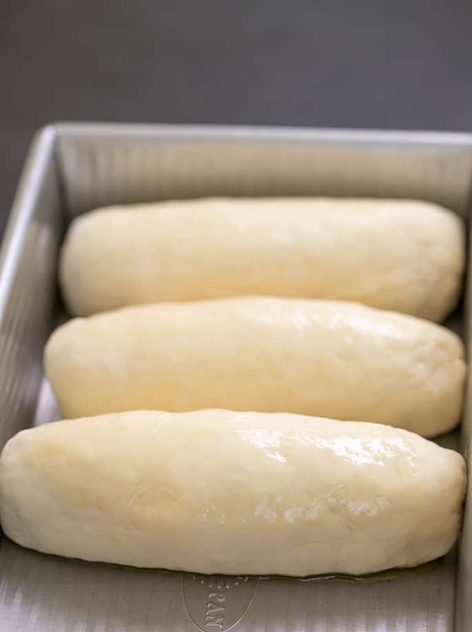 3 Raw Risen Hot Dog Buns in rectangular metal baking pan