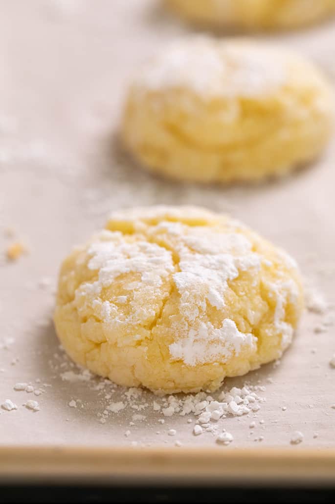 Closeup image of baked round yellow cookies with white powder on white paper on tray