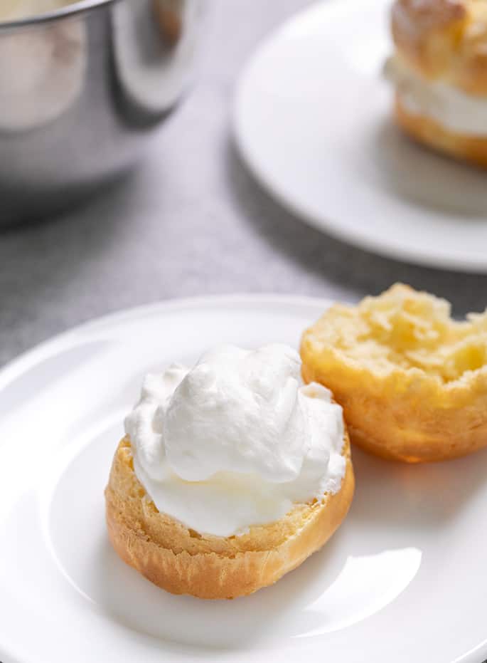 Cream puff pastry on small white plate split open and half filled with whipped cream