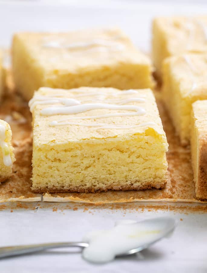 Cut lemon brownies on brown paper with a small spoon with icing in foreground