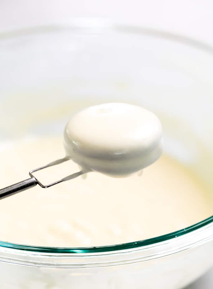 Dipping fork holding Oreo dipped in raw pancake batter held over glass bowl of batter