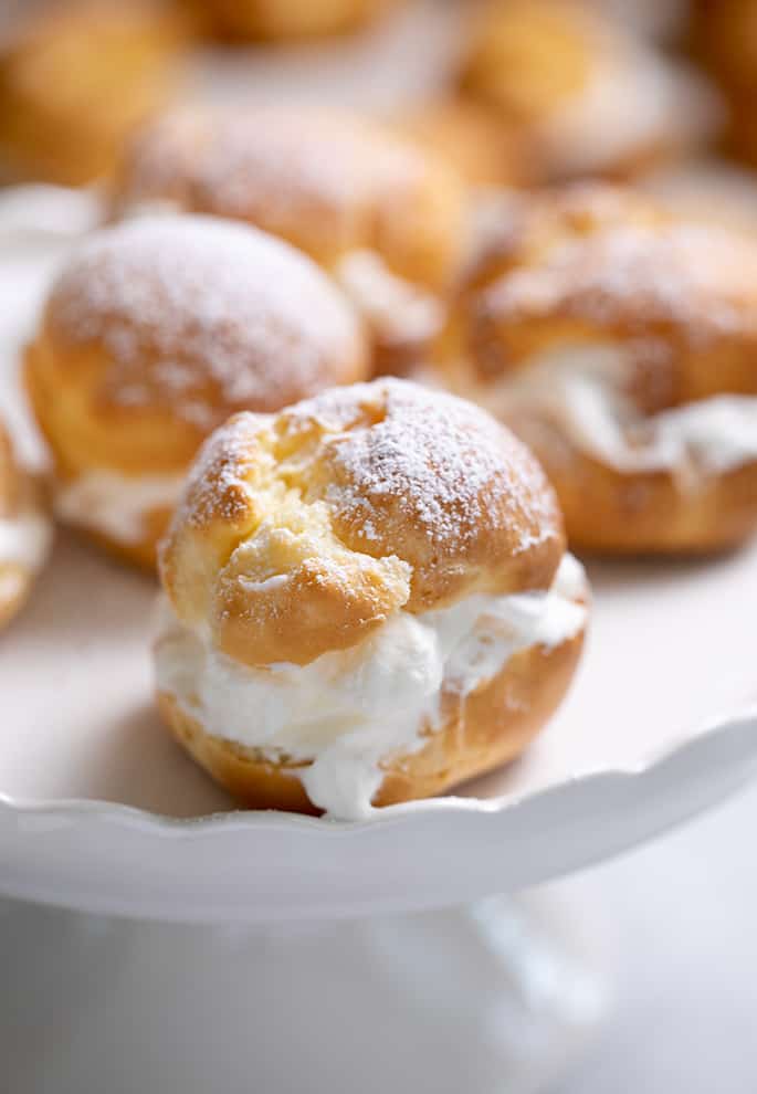 Five cream filled choux pastries with sugar on top on small white cake plate